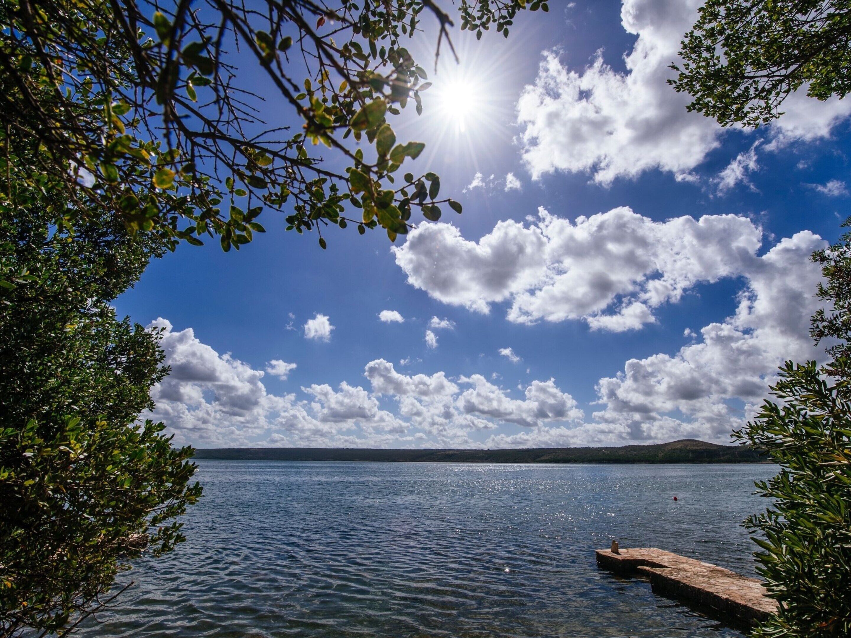 A calm lake with a clear sky and scattered clouds.