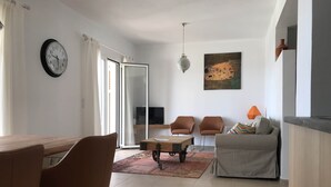 A modern living room with a dining area, a sofa, a coffee table, and a painting on the wall.