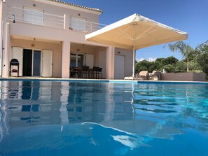A swimming pool with a covered patio area, a dining table, and chairs. - Villa in Finiki With Stunning Sea Views (Pylos-Nestoras)