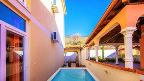 A swimming pool with a clear blue water, surrounded by a building with a tiled roof and white columns. - Alluring Apartment in Dramalj with Hot Tub (Crikvenica)