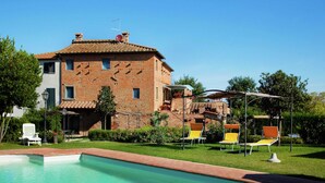 A pool with a clear blue water, surrounded by a brick house with a garden and outdoor seating.