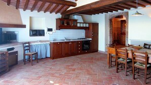 A rustic kitchen with wooden beams, a brick floor, and a dining area with wooden furniture.
