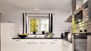 A modern kitchen with white cabinets, a black countertop, a window with curtains, and stainless steel appliances including an oven and microwave. - Cozy Stay Near Durbuy Woods (Durbuy)