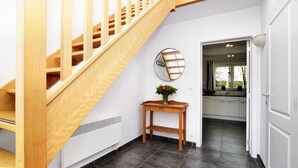 A staircase with wooden railings leading to a kitchen area with dark tiled flooring and a small wooden table with a vase of flowers. - Cozy Stay Near Durbuy Woods (Durbuy)
