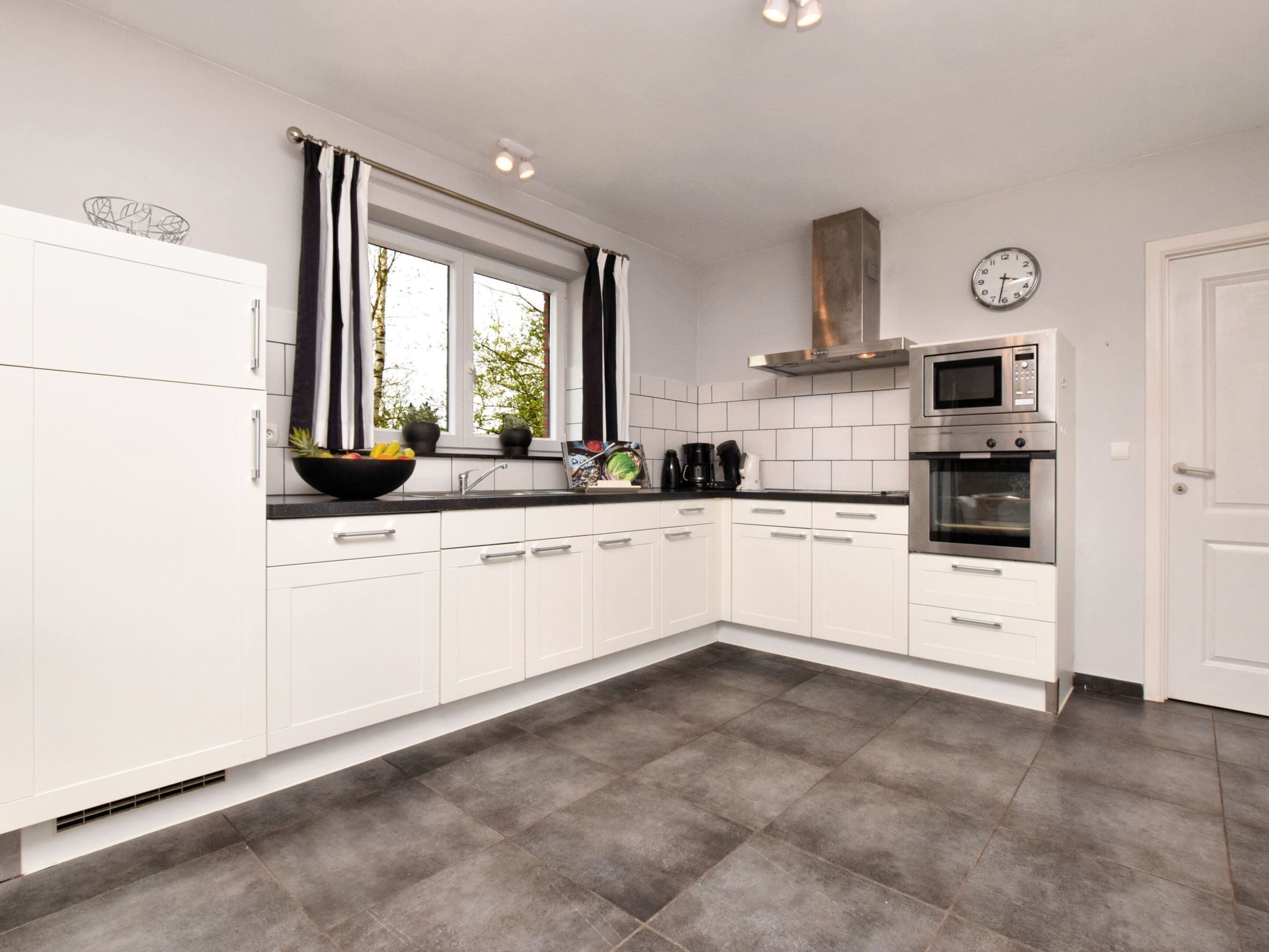 A modern kitchen with white cabinets, a black countertop, a stainless steel oven, and a microwave.