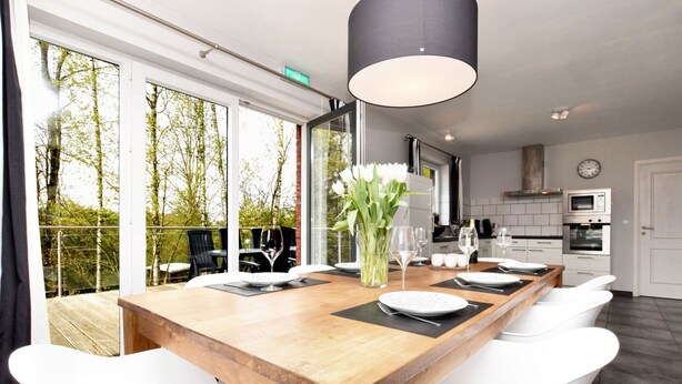 A modern kitchen with a wooden island, white chairs, and a large window overlooking a balcony. - Cozy Stay Near Durbuy Woods (Durbuy)