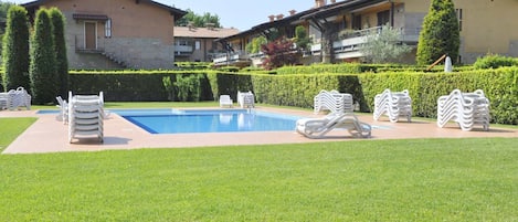 A swimming pool with lounge chairs, neatly trimmed hedges, and a building with balconies.