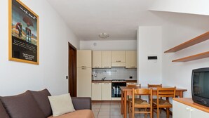 A compact living space with a sofa, a dining table with chairs, a kitchen area with cabinets and a stove, and a television on a wooden stand. - Vibrant Holiday Home in Lazise with Swimming Pool near 2 Lakes (Lazise)