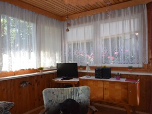 A cozy cabin interior with wooden walls, a television on a wooden table, and a window with lace curtains. - Restful Bungalow in Kühlungsborn near Beach (Kuehlungsborn)