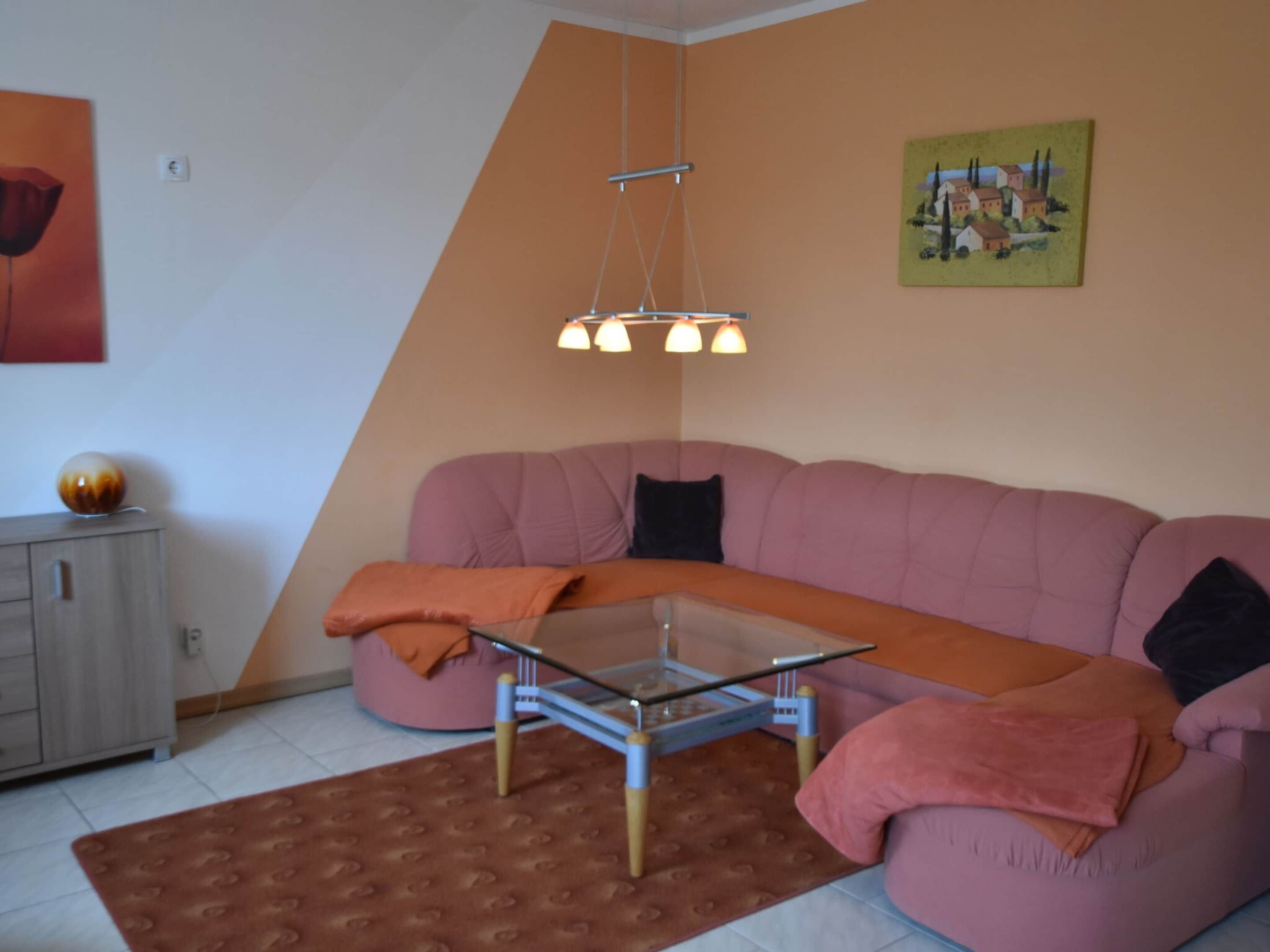 A living room with a pink sofa, a glass coffee table, and a hanging light fixture.