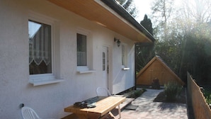 A patio with a wooden table and chairs, a white wall with windows, and a wooden fence.