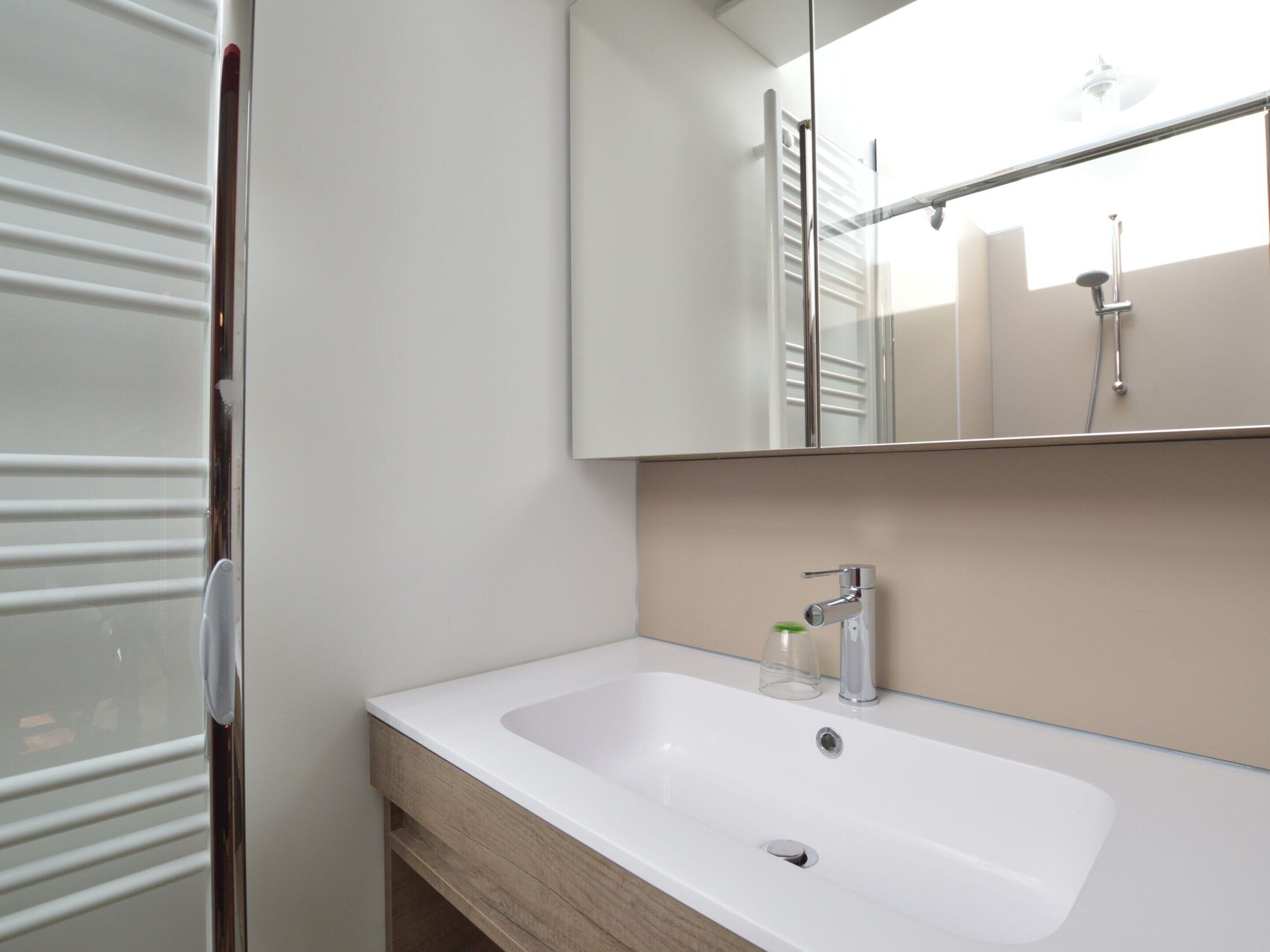 Un baño con un lavamanos blanco, un espejo y una ducha.