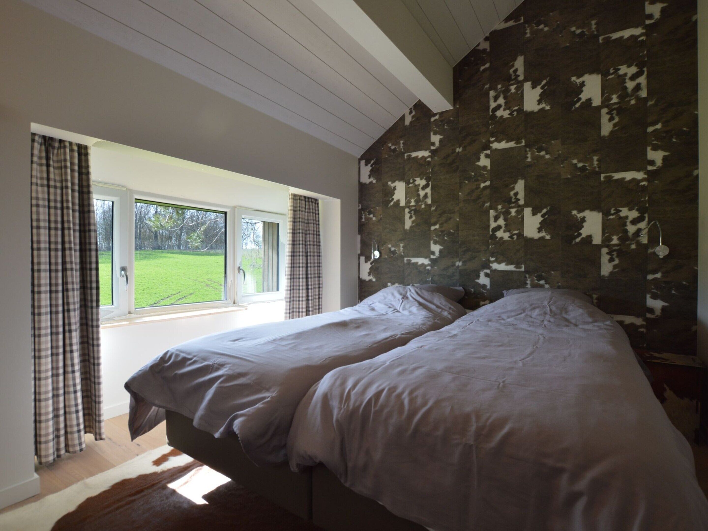 A bedroom with two beds, a large window, and a view of a green landscape.