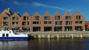 A row of brick buildings with large windows and a docked boat. - Charmante Ferienwohnung in Wismar am Hafen (Wismar)