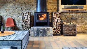 A cozy stone-walled room with a wood-burning stove, a television mounted on the wall, and a rustic wooden table with chairs. - Group Villa With Pool & Sauna (Florenville)