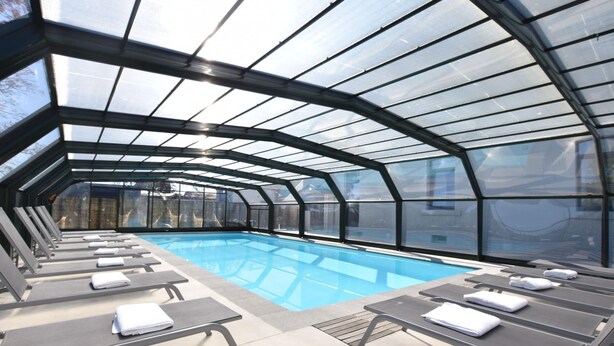 A covered swimming pool with lounge chairs and a glass ceiling. - Group Villa With Pool & Sauna (Florenville)