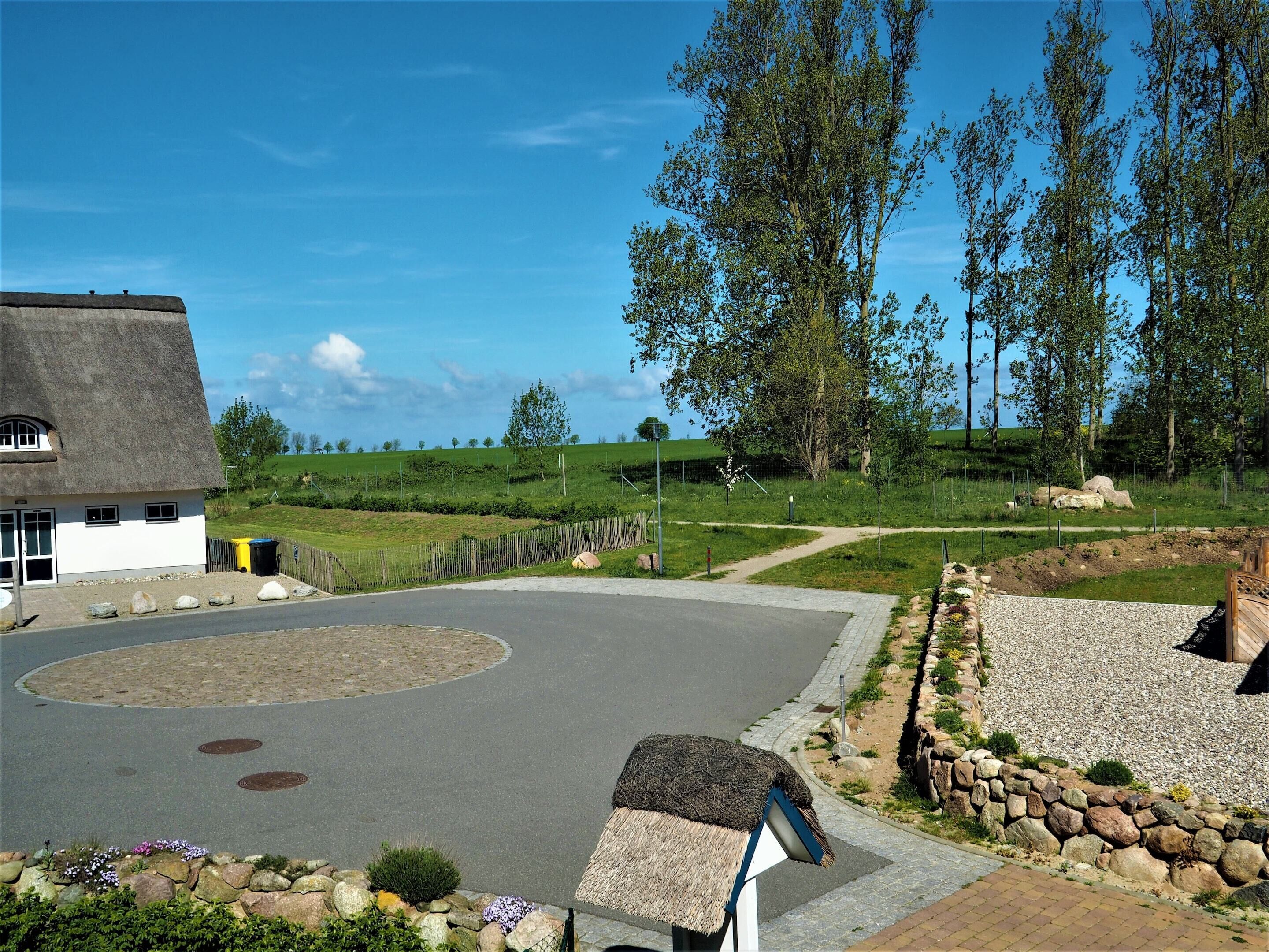 A rural setting with a thatched-roof house, a paved circular driveway, and a stone wall.