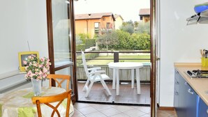 A small balcony with a table and chairs, a view of a residential area, and a kitchen area with a stove and utensils.