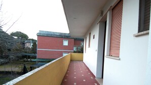 Ein Korridor mit rot-gelben Fliesen, der zu einem Gebäude mit roter Fassade und einem Fenster mit braunen Fensterläden führt.