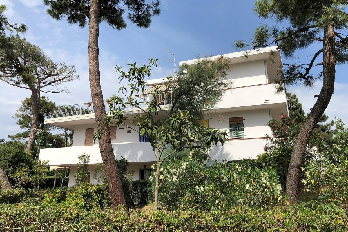 A two-story building with balconies, surrounded by trees and vegetation.