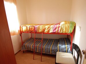 A bunk bed with colorful bedding, a chair, and a door.