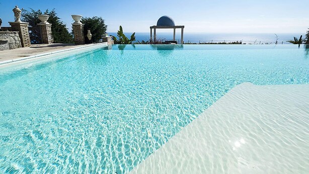 A clear blue infinity pool with a gazebo and a view of the ocean. - Exclusive Villa With Panoramic Swimming Pool and Hot Tub, Near the Sea (Letojanni)
