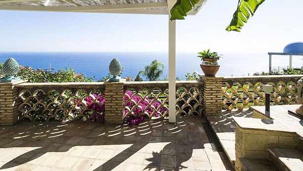 A covered outdoor area with a view of the sea, featuring a tiled floor, a decorative fence, and potted plants. - Exclusive Villa With Panoramic Swimming Pool and Hot Tub, Near the Sea (Letojanni)