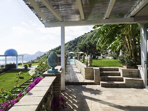 A covered outdoor area with a pool, steps leading to a building, and a view of mountains.