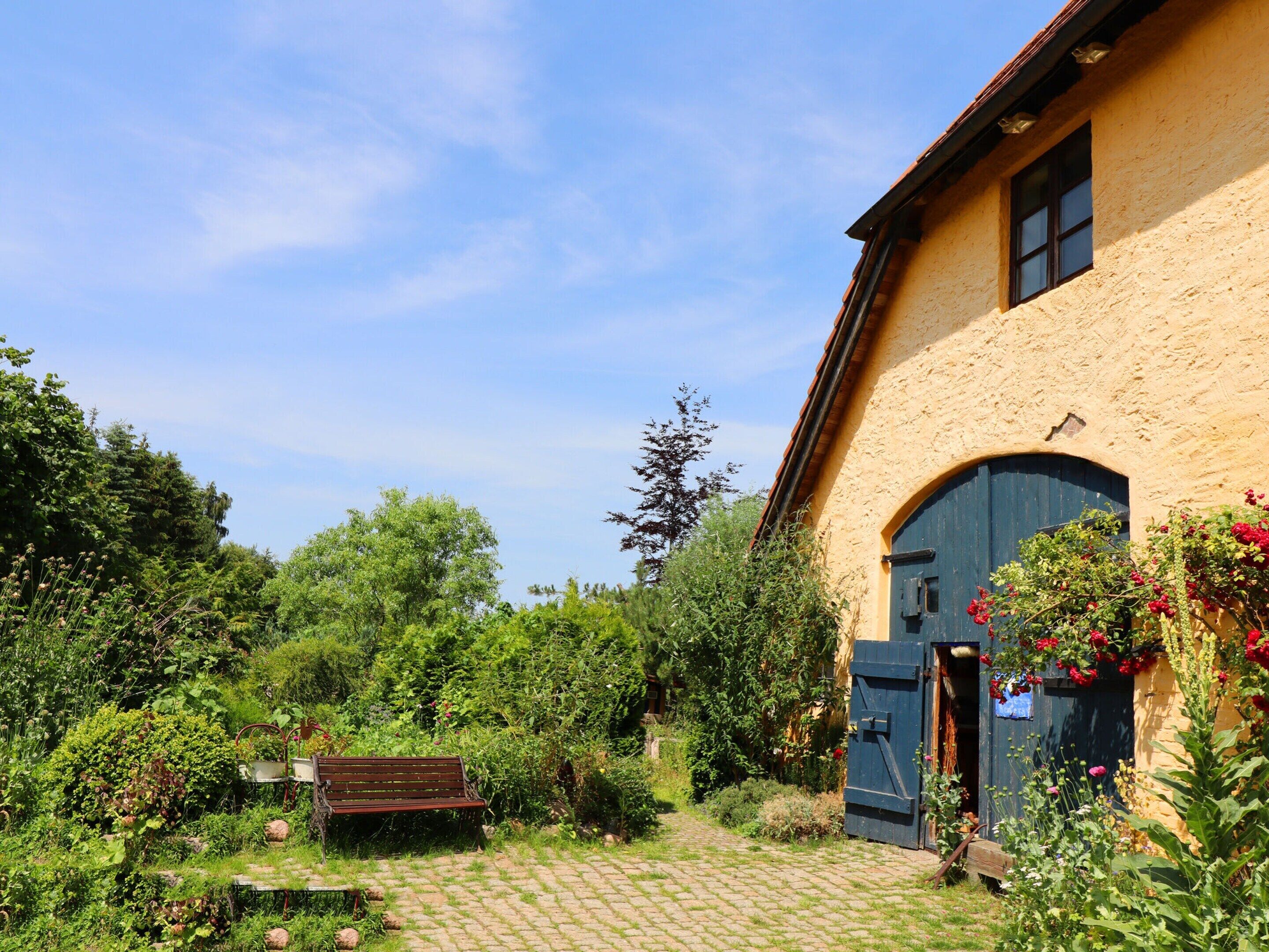 A rustic building with a blue door, surrounded by lush greenery and a cobblestone path.