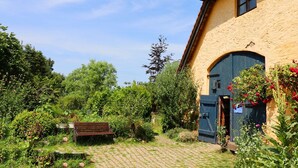 A rustic building with a blue door, surrounded by lush greenery and a cobblestone path. - Ferienwohnung Parkblick mit 3 Schlafzimmern (Niepars)