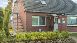 A two-story brick house with a tiled roof, a visible chimney, a small window, and a door. There is a stone wall with plants in front of the house. - Moderne Ferienwohnung in Meeresnahe in Tarnewitz (Boltenhagen)