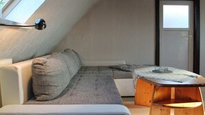 A cozy attic bedroom with a sloped ceiling, a sofa, a wooden table, and a door. - Moderne Ferienwohnung in Meeresnahe in Tarnewitz (Boltenhagen)