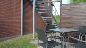 A brick building with a metal staircase, outdoor seating with metal chairs and a table, and a wooden fence. - Moderne Ferienwohnung in Meeresnahe in Tarnewitz (Boltenhagen)
