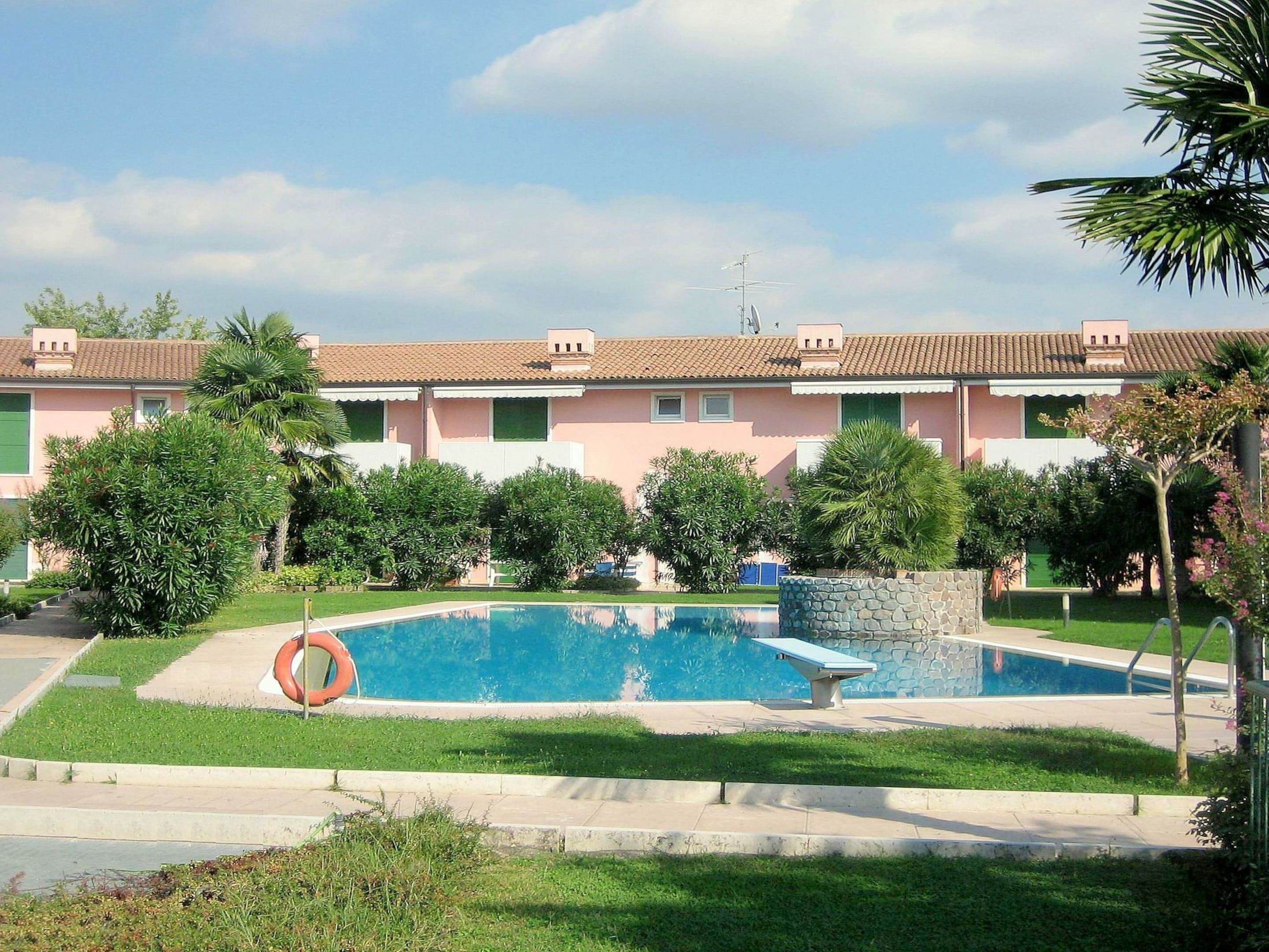 Ein Wohngebäude mit Schwimmbad, umgeben von Grünflächen und einem wolkenlosen Himmel.