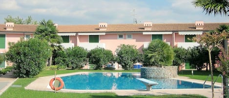 A residential building with a swimming pool, surrounded by greenery and a clear sky.