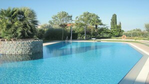 A clear swimming pool with a stone wall and palm trees. - Vibrant Holiday Home in Lazise with Swimming Pool near Lake (Lazise)