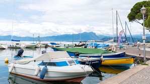 A marina with various boats docked, a paved walkway, and mountains in the background. - Vibrant Holiday Home in Lazise with Swimming Pool near Lake (Lazise)