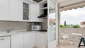 A compact kitchen with white cabinets, a Bosch dishwasher, a microwave, and a gas stove. There's a sliding glass door leading to an outdoor seating area with a table and chairs. - Vibrant Holiday Home in Lazise with Swimming Pool near Lake (Lazise)