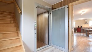 Ein modernes Interieur mit einer Holztreppe, einer Schiebetür zu einem Küchenbereich und einem sichtbaren Aufzug.