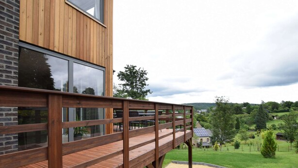 Ein modernes Gebäude mit einer Holzdiele und Glasfenstern, die auf eine grüne Landschaft blicken.