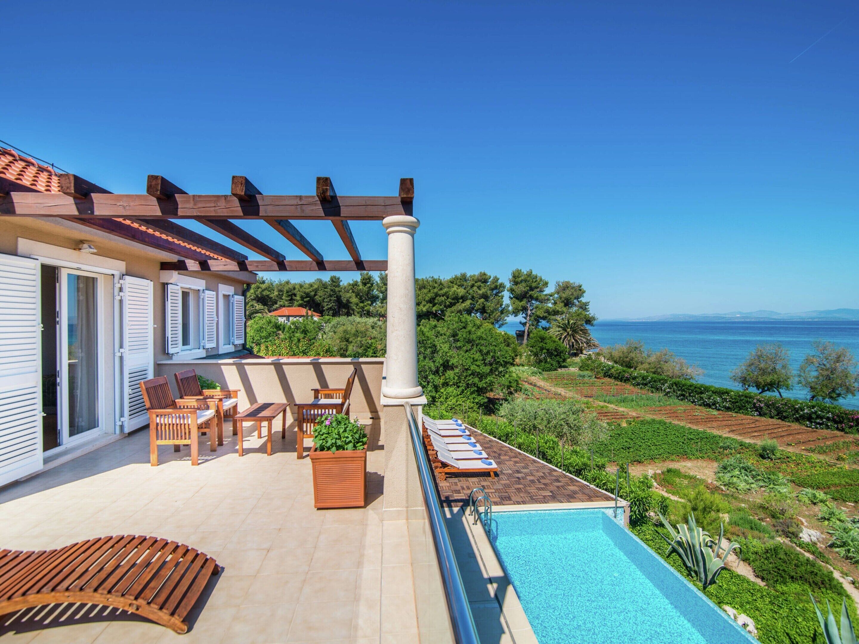 A poolside area with a pergola, outdoor seating, and a view of the sea.