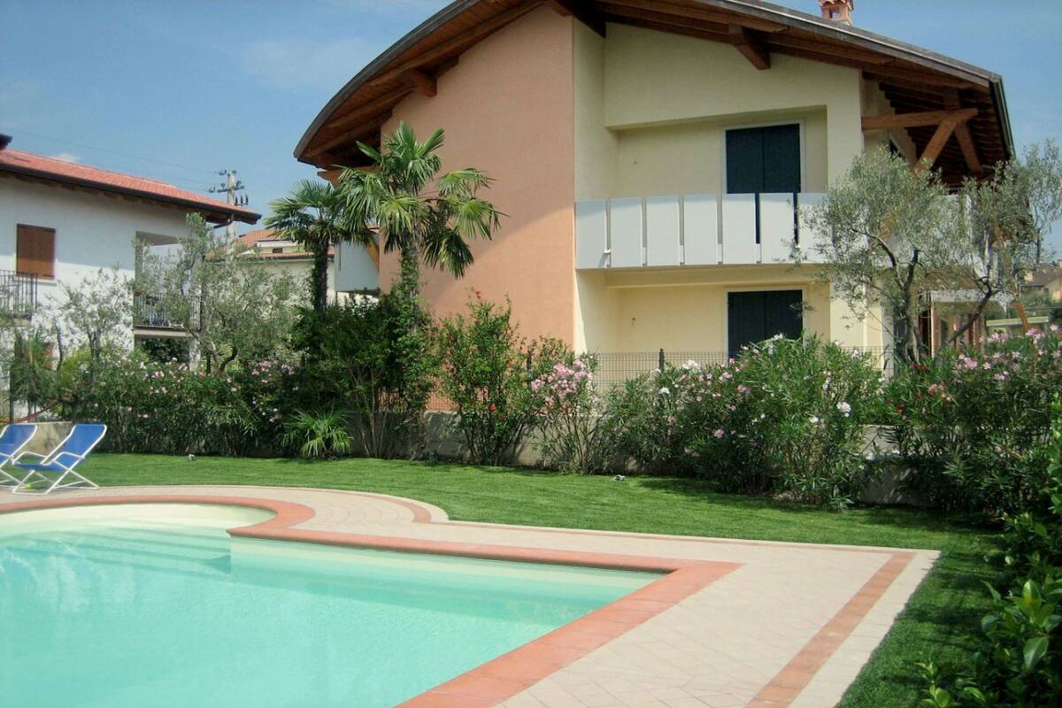 Ein zweistöckiges Gebäude mit Swimmingpool, umgeben von einem gepflegten Garten mit verschiedenen Pflanzen und Blumen.