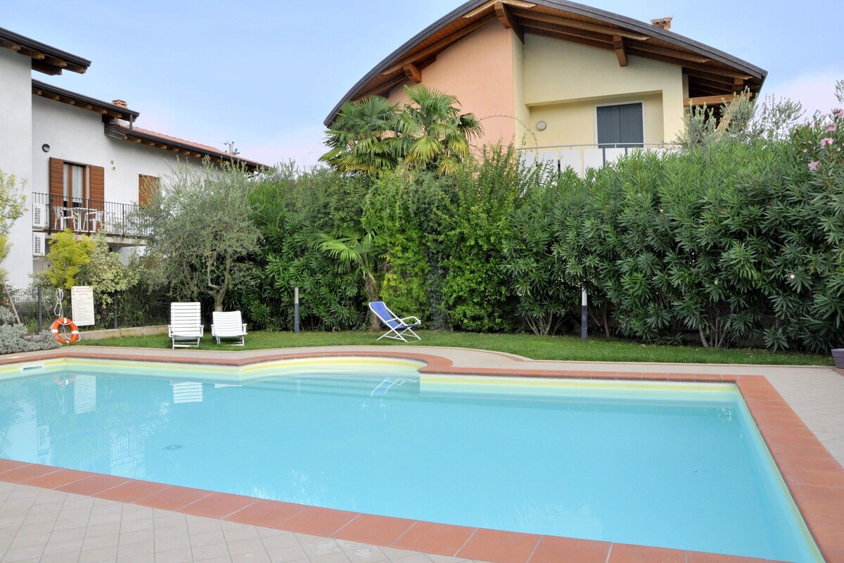A swimming pool with a lifebuoy, lounge chairs, and a building with a balcony in the background.
