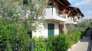 Un immeuble résidentiel à plusieurs étages, doté de balcons et entouré d’une végétation luxuriante.