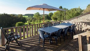 A wooden deck with a table and chairs, an umbrella, and a view of a green landscape. - Cottage in a Well-equipped and Comfortable Farmhouse (Marche-en-Famenne)