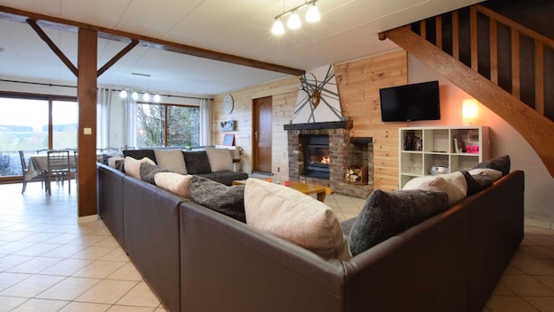 A cozy living room with a fireplace, a sofa, a dining area, and a staircase. - Cottage in a Well-equipped and Comfortable Farmhouse (Marche-en-Famenne)