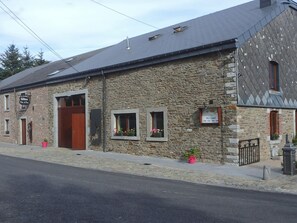 A stone building with a sloped roof, a wooden door, and small windows with flower boxes. - Cottage in a Well-equipped and Comfortable Farmhouse (Marche-en-Famenne)