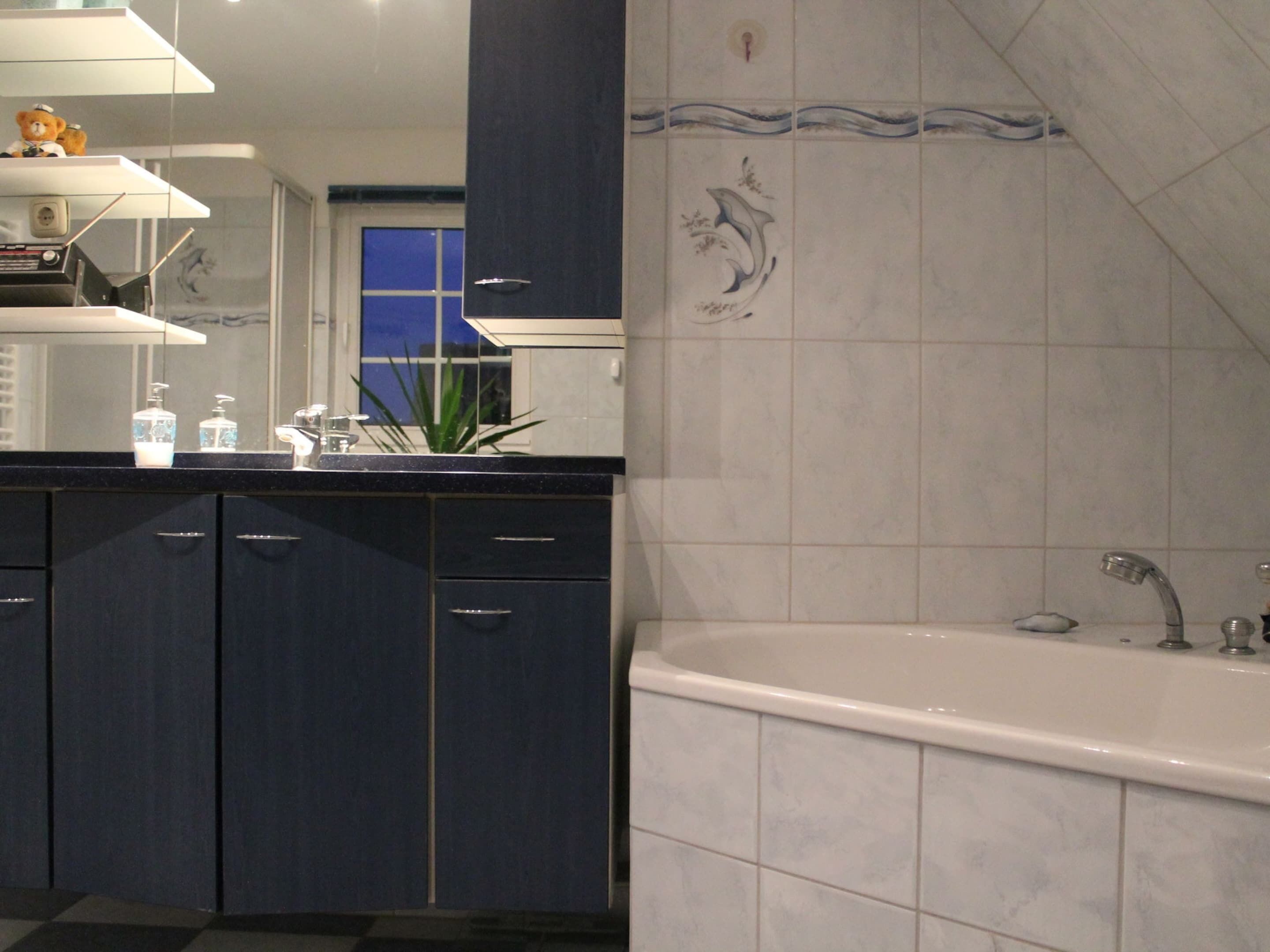 A modern bathroom with a bathtub, dark blue cabinets, and a decorative tile backsplash.