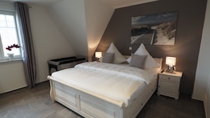Ein Schlafzimmer mit einem großen Bett, zwei Nachttischen mit Lampen, einem Fenster mit Vorhängen und einem Bild an der Wand.