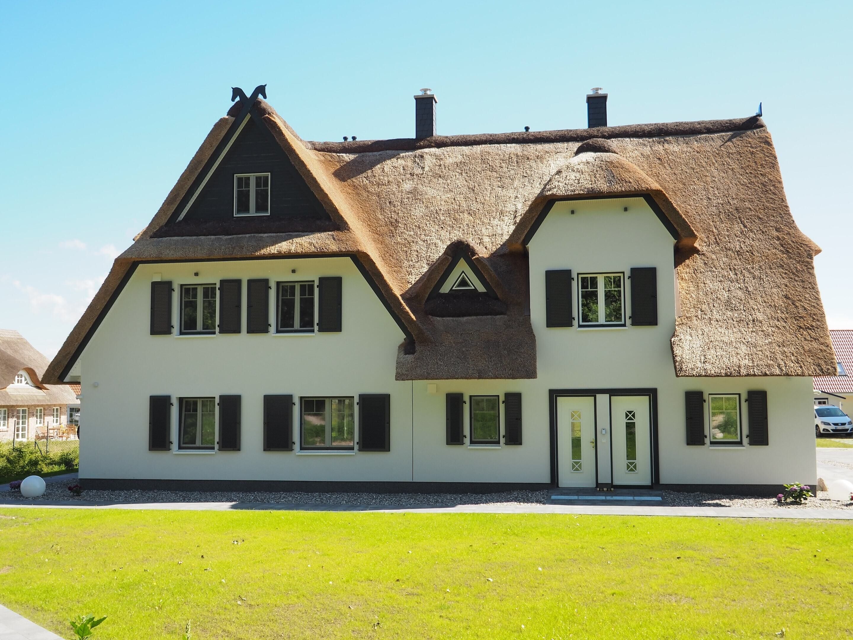 Une maison traditionnelle avec un toit de chaume, des murs blancs et des volets noirs.